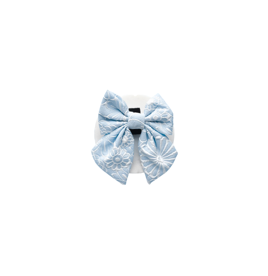 A Cocopup London Baby Blue Flower LUXE Sailor Bow Tie, arranged on a white marble-like surface with scattered pastel flower confetti. 