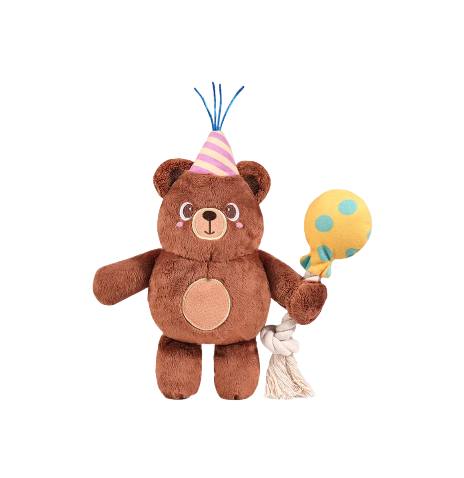 A Hugsmart Yappy Birthday Party Bear Dog Toy, wearing a pink and yellow striped party hat with blue tassels, on a plain white background.