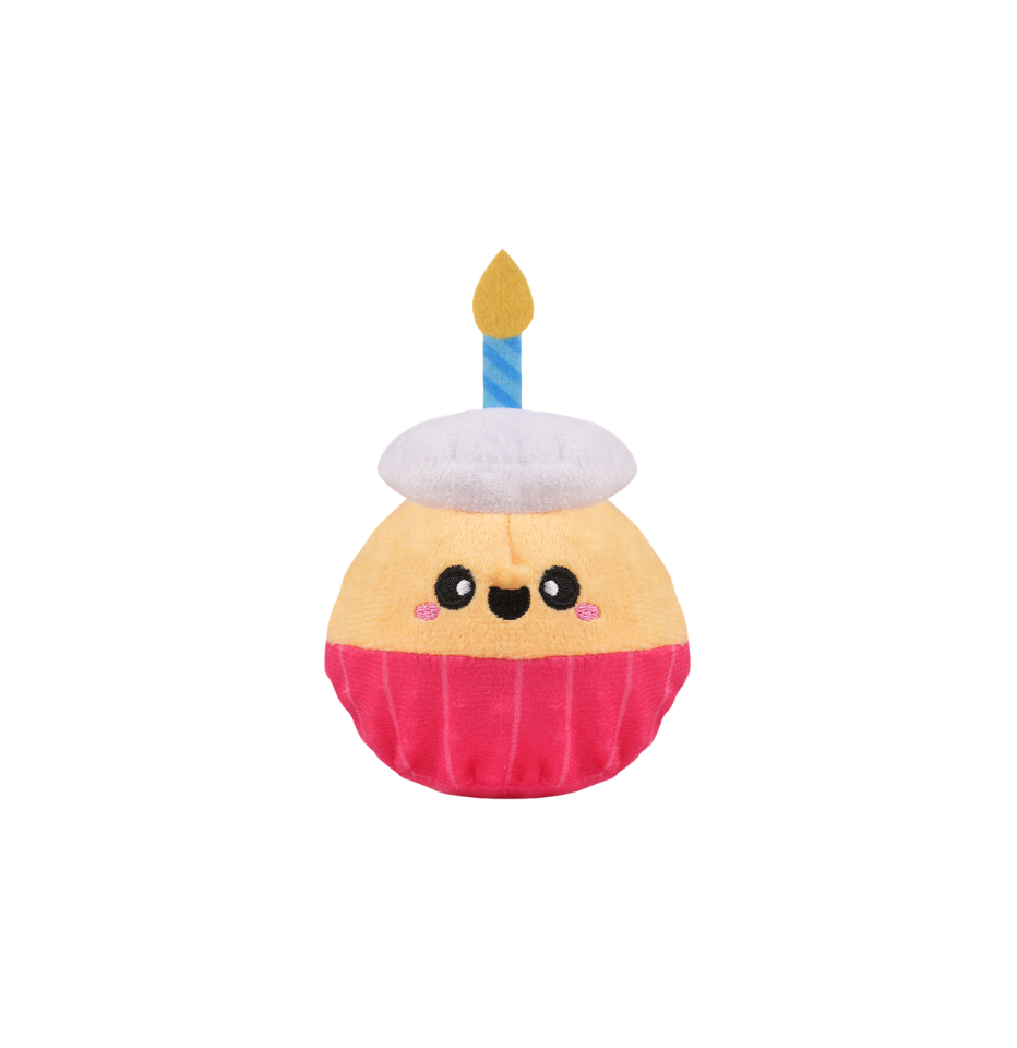 A Hugsmart Yappy Birthday Super Ball Cupcake Dog Toy with a smiling face, featuring a beige frosting top, a white frosting hat, a pink wrapper, and a single blue candle with a yellow flame, isolated on a white background.