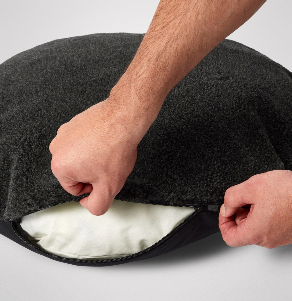 Hands unzipping the cover of the MiniJumbuk Sleep Calm Oasis Wool Dog Bed in storm grey, revealing the removable insert underneath