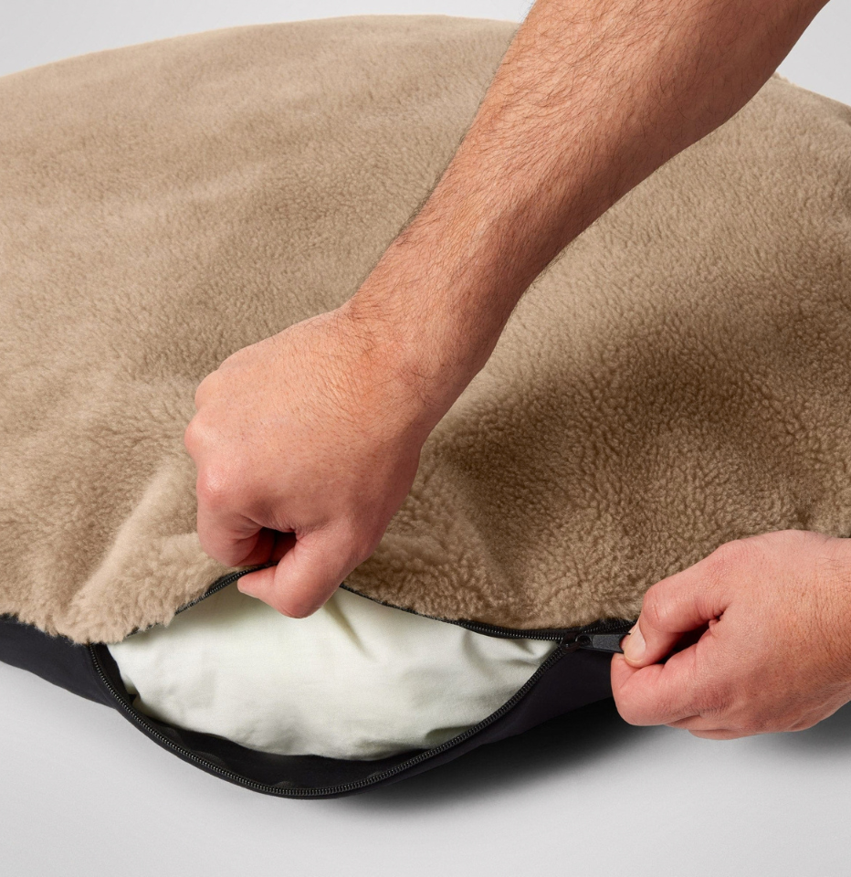 Hands unzipping the cover of the MiniJumbuk Sleep Calm Oasis Wool Dog Bed in fawn, revealing the removable insert underneath